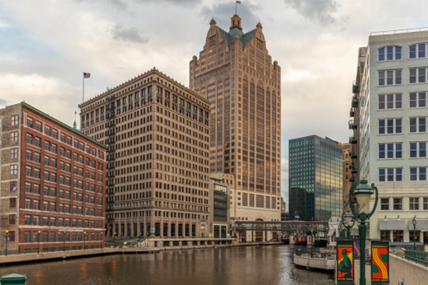 Spring view of the Milwaukee RiverWalk with blooming trees and downtown Milwaukee skyline.